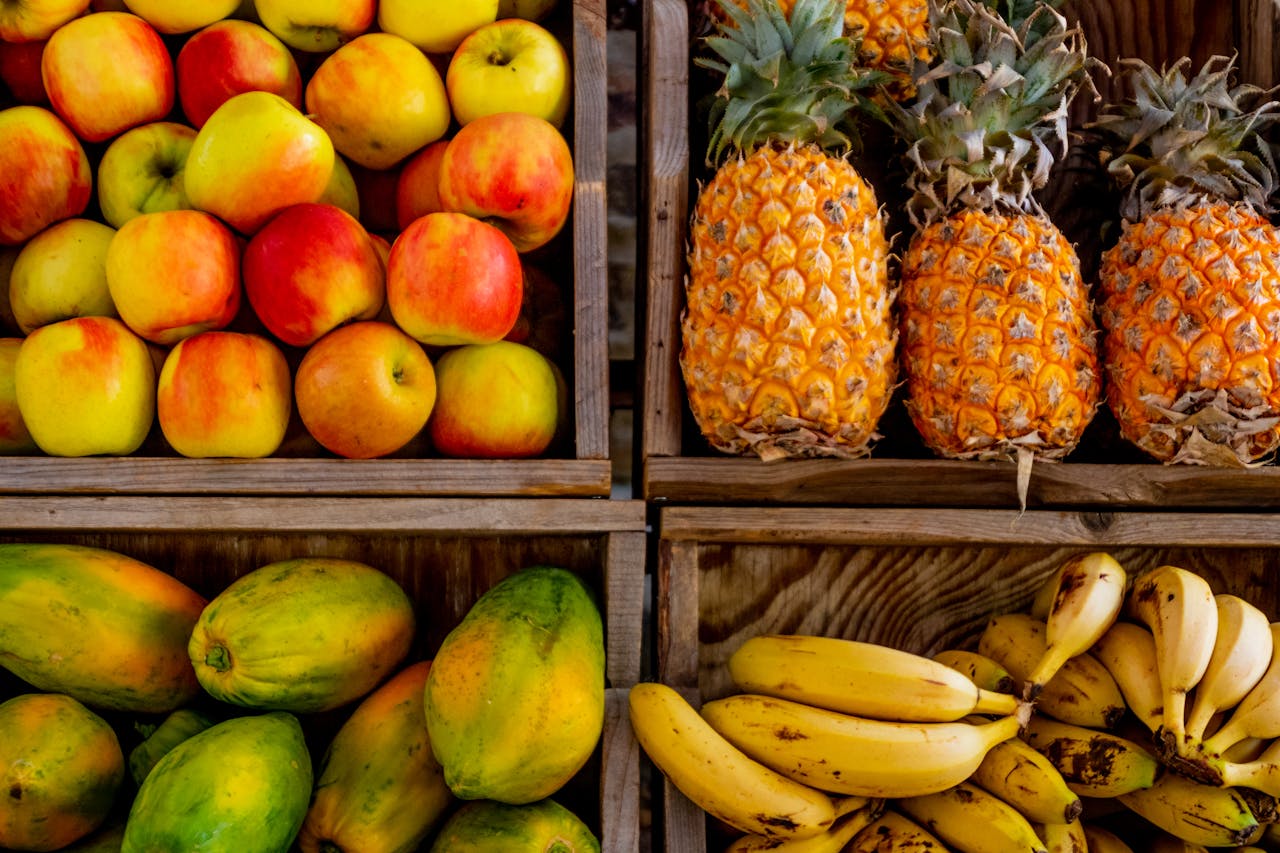 services-01 Colorful display of apples, pineapples, bananas, and papayas in wooden crates at a market.