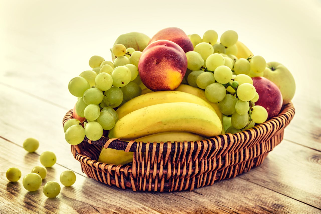 gallery-3 A colorful wicker basket filled with fresh grapes, bananas, and apples on a wooden table.