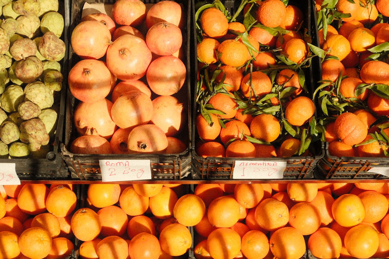 hero-img-02 Colorful assortment of citrus fruits and pomegranates at a bustling Lisbon market.