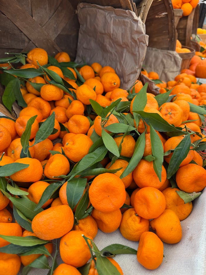 services-img A vibrant display of fresh oranges with leaves, set in wooden baskets at an outdoor market.